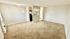 Bright and spacious living room with plush carpeting, leading to an open kitchen area through a stylish partition. Neutral tones enhance the airy feel, perfect for modern living.