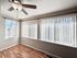 Bright sunlit room with hardwood flooring and modern ceiling fan, featuring large windows with vertical blinds.