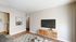 Cozy living room with modern decor, featuring a sleek TV setup, wooden floors, and open access to a quaint kitchen.