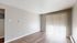 Bright and inviting empty room with sleek wooden flooring and large window featuring vertical blinds, perfect for customization.