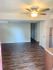 Inviting apartment interior with sleek wooden floors and ample natural light, featuring a modern ceiling fan and a transition to a cozy kitchen area.