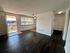 Bright open living space with dark hardwood floors, large window, and a cozy entryway leading to a balcony view.