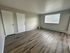 Bright and spacious room with modern hardwood floors, large window for natural light, and two white doors. Perfect for versatile living arrangements.