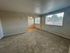 Bright and inviting living space with large windows, plush carpeting, and an open doorway leading to a cozy dining area.
