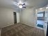Bright, freshly carpeted bedroom with ceiling fan, spacious closet, and open entry to sunlit living area.