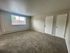Bright and spacious living room with plush carpeting, large window offering natural light, and two white doors for convenient access.