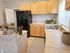 Charming kitchen with natural wood cabinets, sleek black fridge, and cozy dining area, complemented by a sunlit window and modern decor.
