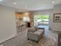 Inviting open-concept living room with modern kitchen, cozy gray sofa, bar seating, and glass doors leading to a sunny balcony with a scenic view.