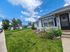 Charming single-story white cottages with well-maintained lawns and blooming sunflowers under a bright blue sky.