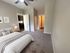 Inviting bedroom with plush carpeting, stylish bed setup, and soft lighting, leading to a modern kitchen area.