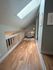 Cozy loft area with wooden flooring, a plush armchair, and natural skylight illuminating the space, perfect for relaxation.