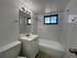 Modern bathroom with sleek white fixtures, a bathtub, large mirror, and natural light from a window.