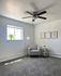 Bright, modern bedroom with cozy grey carpet, stylish armchair, and decorative wall art, featuring natural light and a ceiling fan for comfort.