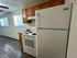 Modern kitchen with hardwood flooring, featuring a white refrigerator, electric stove, and warm wooden cabinetry, complemented by natural light from large windows.