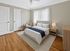 Inviting bedroom with soft lighting, modern neutral decor, wooden floors, and a cozy chair. Ideal for comfort and relaxation.