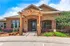 Charming brick apartment exterior boasting a welcoming arched entry, vibrant landscaping, and rustic wooden pergola, against a bright blue sky.