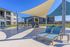 Modern outdoor lounge area featuring stylish sun loungers, large shade sails, and a cozy fireplace, perfect for relaxation and entertaining.