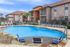 Inviting outdoor pool area with stylish seating, surrounded by well-maintained landscaping and modern apartment buildings under a clear blue sky.