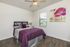 Cozy bedroom with a plush purple bedspread, wooden flooring, and elegant wall art creating a tranquil atmosphere.