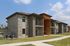 Elegant two-story apartment building with modern brick and siding exterior, featuring private balconies and well-maintained landscaping under a clear blue sky.