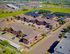 Aerial view of a charming, well-planned apartment complex with red brick buildings, ample parking, and lush green surroundings, offering a serene residential experience.