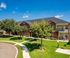 Charming brick apartment complex with lush green lawns and mature trees under a clear blue sky.