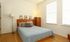 Bright bedroom with stylish wooden furniture, soft bedding, and ample natural light from two large windows.