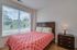 Bright bedroom with large window, featuring a stylish bed and bedside table, offering a view of greenery outside.