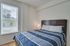 Inviting bedroom with large window, a comfortable bed with blue striped bedding, and soft lighting.