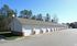 Long row of modern garage units with white doors, set against a backdrop of tall trees and clear blue sky.