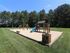Charming outdoor playground with swings, slide, and climbing structure surrounded by lush greenery.