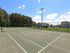 Spacious tennis court surrounded by greenery and residential buildings under a clear blue sky.