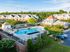 Elegant apartment complex with a large swimming pool and lush greenery, featuring modern architecture and vibrant amenities.