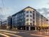 Contemporary urban apartment complex at dusk with bright signage, modern design, and street view.