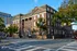 Elegant brick apartment building with classic architectural design and lush trees at a city intersection.