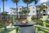 Inviting outdoor firepit area with green chairs set against modern white apartments and palm trees.