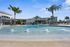 Sunny pool area with palm trees and a modern building backdrop.