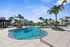Spacious resort-style pool surrounded by palm trees and modern apartments under a bright blue sky.