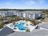 Aerial view of a modern apartment complex featuring a large, stylish swimming pool surrounded by palm trees and lush green landscaping.