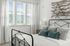 Bright bedroom with large window, metal bed frame, and decorative wooden wall art.
