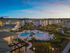 Evening view of a luxurious apartment complex featuring a central swimming pool surrounded by beautifully landscaped gardens and palm trees.