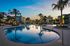 Elegant evening view of a luxurious apartment complex with a sparkling swimming pool surrounded by palm trees.