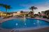 Elegant apartment complex with illuminated swimming pool and lush palm trees at twilight.