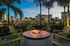 Elegant outdoor seating area with fire pit surrounded by tropical palm trees and modern apartments at dusk.