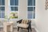 Bright reading nook with modern chair, plaid pillow, and small round table beside large windows.