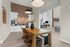 Stylish dining area with wicker chairs and wooden table, accent wall decor, and a view into a spacious living area.