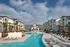 Elegant apartment complex featuring a pristine pool, surrounded by palm trees and modern architecture.
