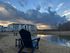 Charming lakeside apartment complex with Adirondack chairs, reflecting a picturesque sunset sky.
