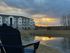 Charming apartment complex by a tranquil pond at sunset, with a scenic view and comfortable outdoor seating.