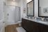 Modern bathroom with double vanity, granite countertops, and a sleek bathtub wrapped in elegant tiles.